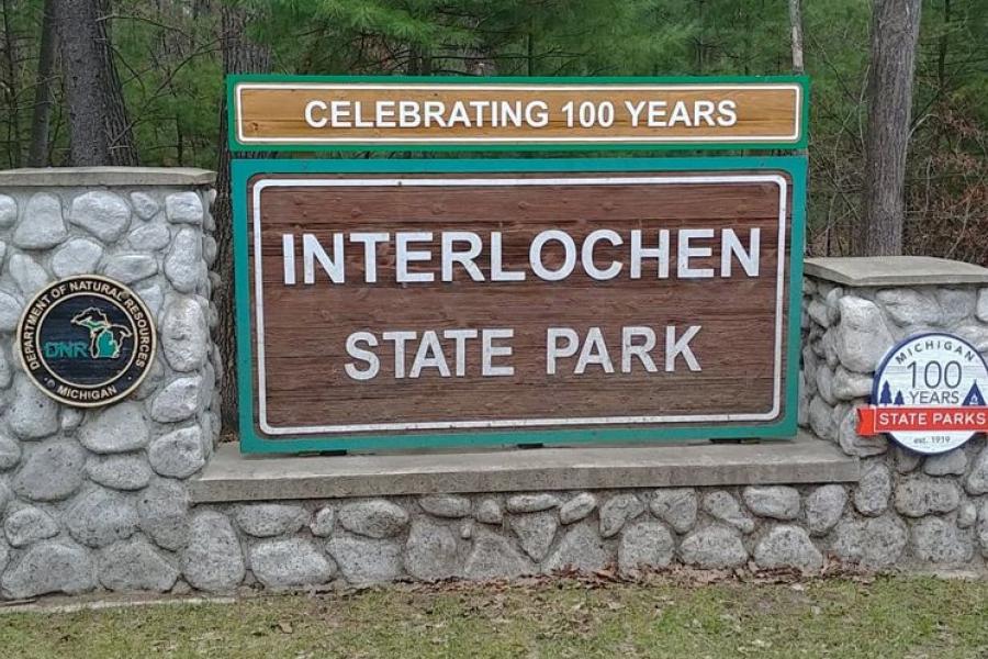 The current Interlochen State Park sign with centennial plaques